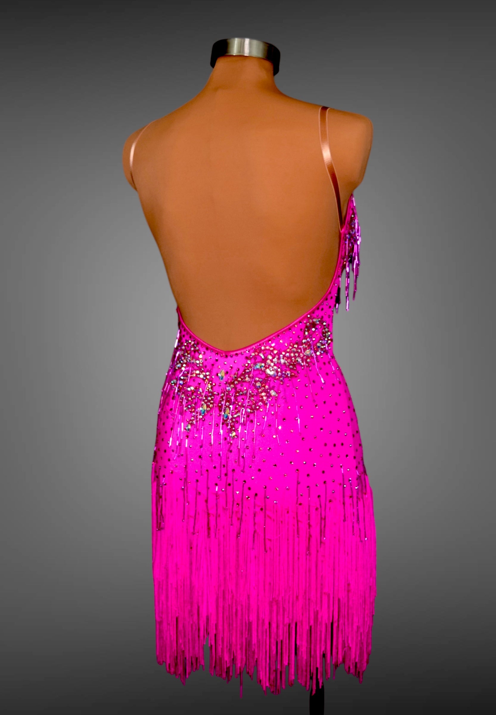 Mannequin wearing a bright pink dress with fringe and sequins on a gray background