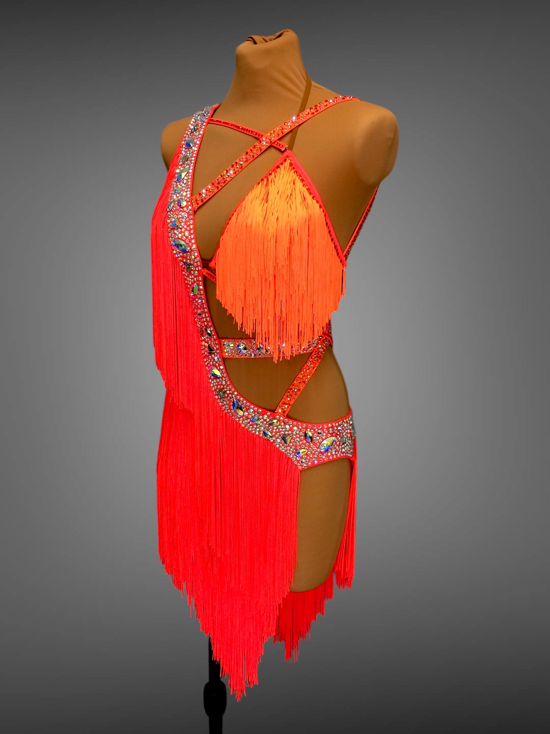 Orange fringe dress with embellishments on a mannequin against a gray background