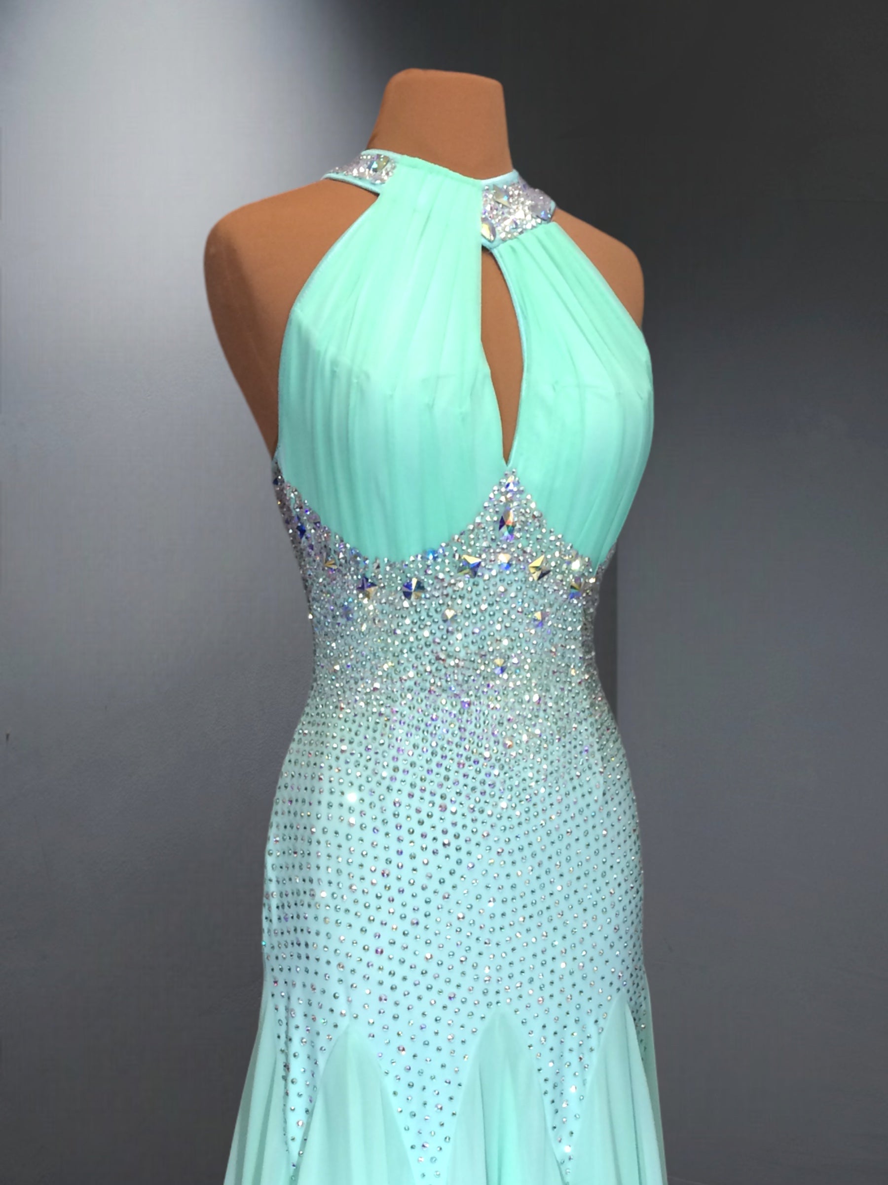 Mint green evening gown with beaded details on a mannequin against a gray background