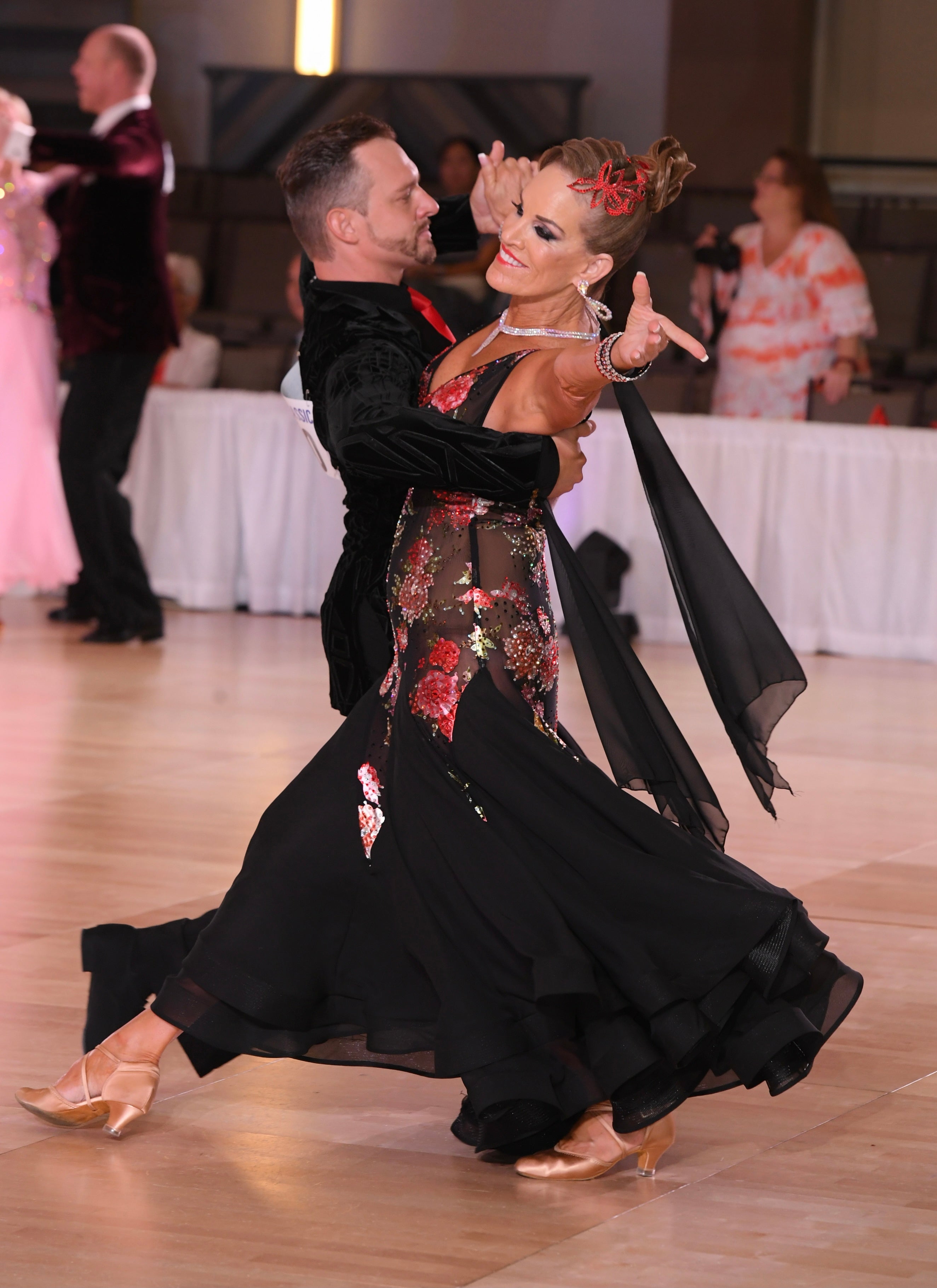 Dancers in formal attire performing a ballroom dance on a wooden floor.