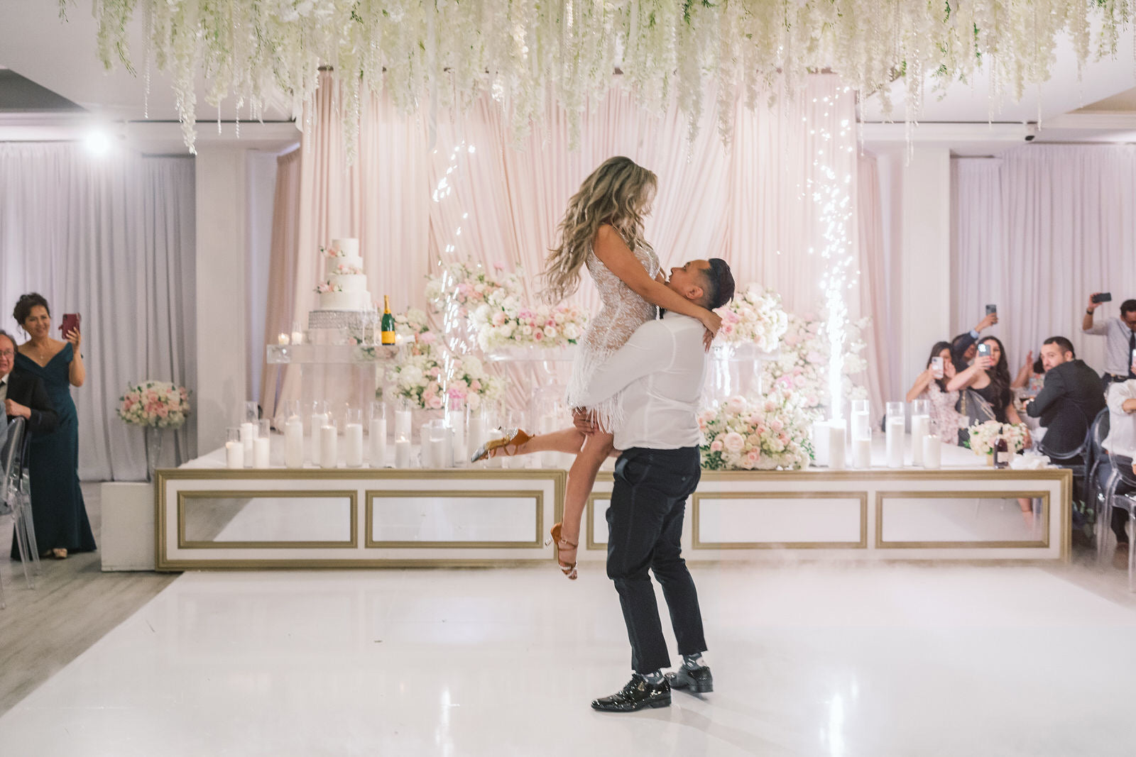 Man lifting a woman in a decorated indoor setting with floral arrangements and candles.