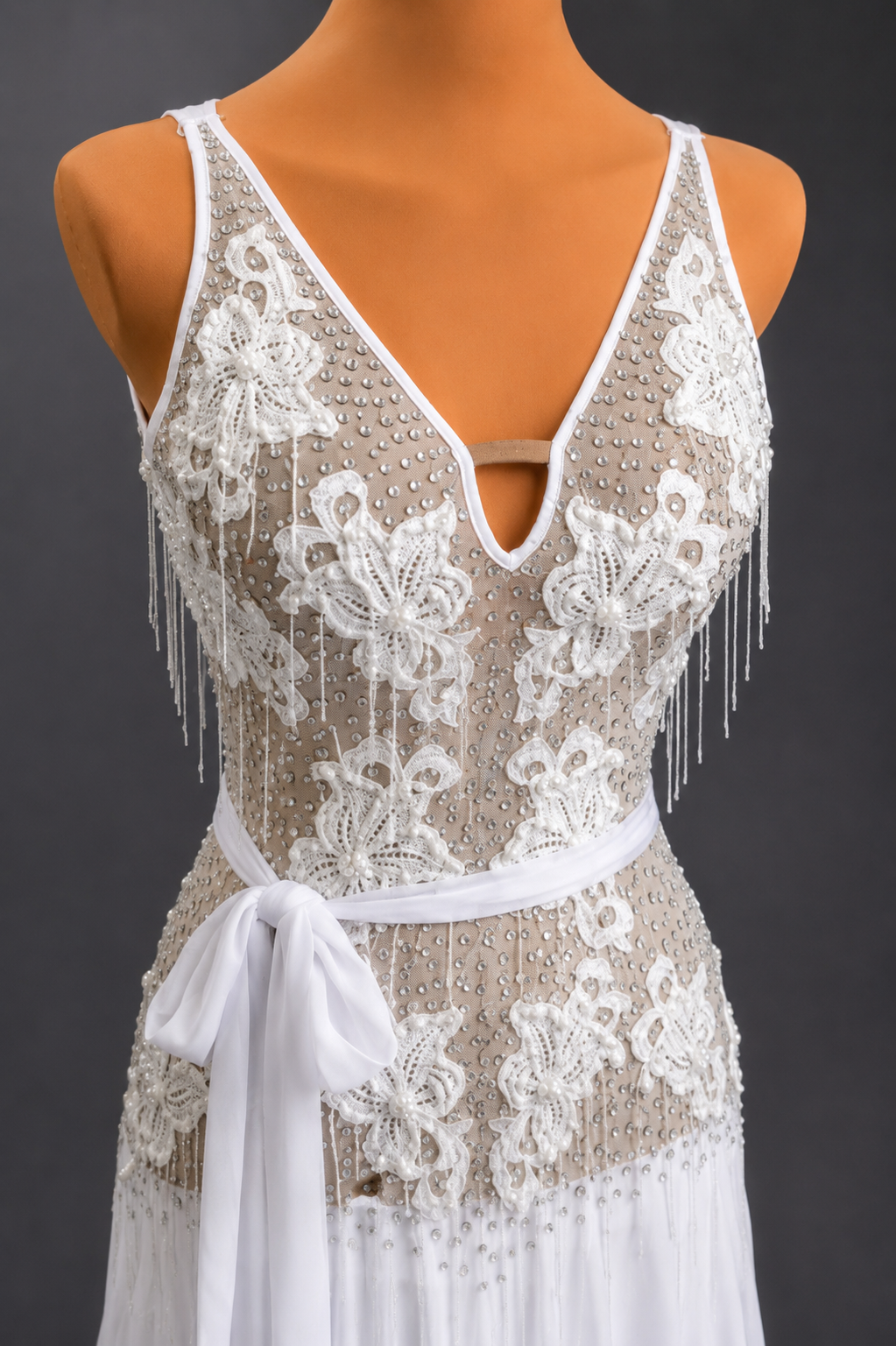 Lace dress with white fringes on a mannequin against a dark background