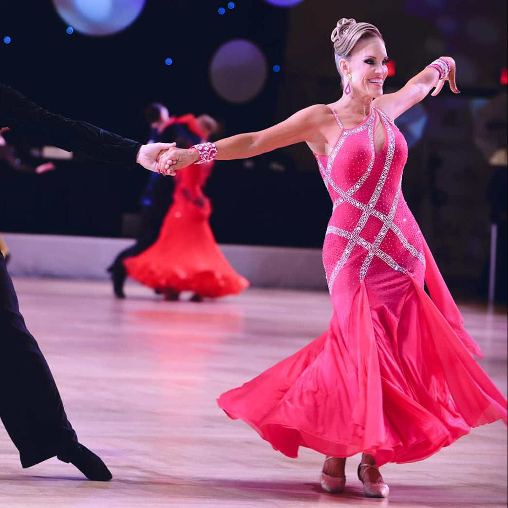 Dancers in vibrant pink ballroom competition dress  performing on a dance floor